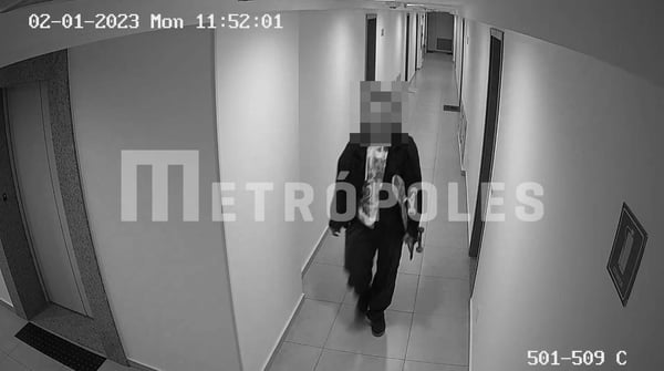 Imagem de câmera de segurança, em preto e branco, mostra jovem andando por corredor, com skate na mão. Ele usa roupas escuras, camisa clara e tem o rosto borrado