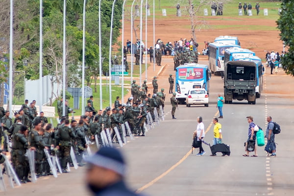 Agentes da PMDF e Exército desocupam acampamento bolsonarista no QG do Exército, em Brasília. Ao lado direito, percebe-se uma barreira de contenção de militares e ao fundo, vários ônibus levando detidos os terroristas que participaram da destruição da Esplanada - Metrópoles