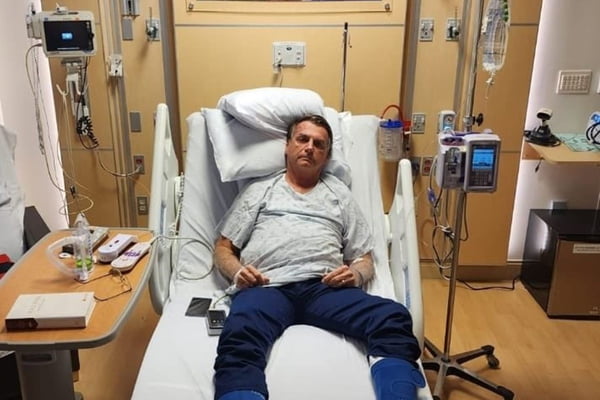 O ex-presidente Jair Bolsonaro aparece deitado em cama de hospital, com roupas hospitalares e uma sonda acoplada ao braço. Ele parece cansado, durante internação por desconforto abdominal nos Estados Unidos - Metrópoles