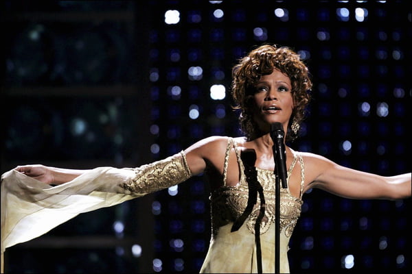 Whitney Houston cantando com look dourado - Metrópoles