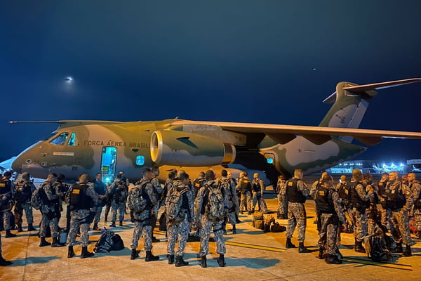 Policiais da Força Nacional junto a avião da FAB, de noite, em local de aéreo desembarcando em Roraima - Metrópoles