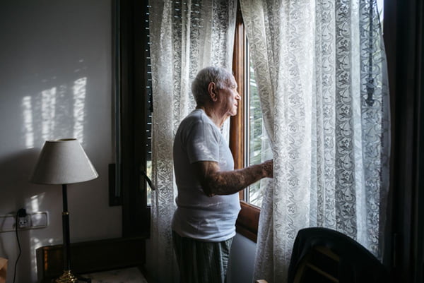 Imagem colorida: idoso observa a rua pela janela - Metrópoles