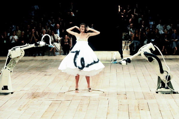 Na passarela da marca Alexander McQueen, modelo usa vestido branco que é pintado por máquinas com tinta - Metrópoles