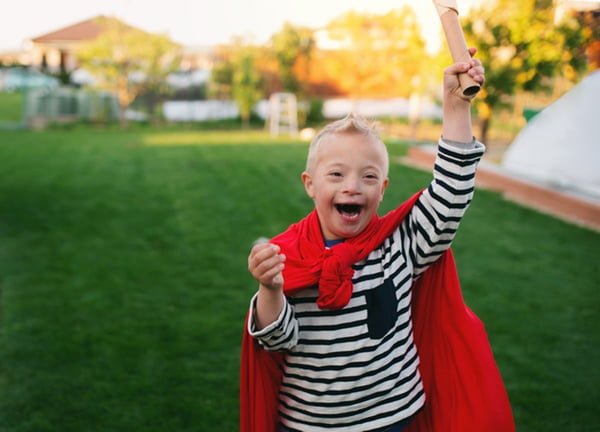Imagem colorida: menino com síndrome de Down veste capa vermelha - Metrópoles