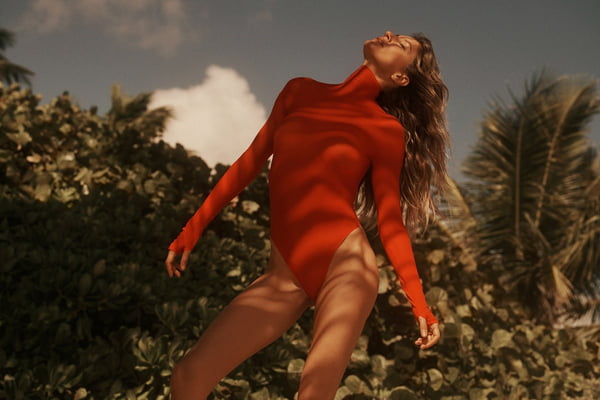 A modelo Gisele Bündche, uma mulher branca e de meia idade, com cabelo loiro ondulado, posa para foto em praia na Costa Rica. Os cliques são da revista Vanity Fair. Gisele veste um maiô de mangas longas na cor vermelha. - Metrópoles