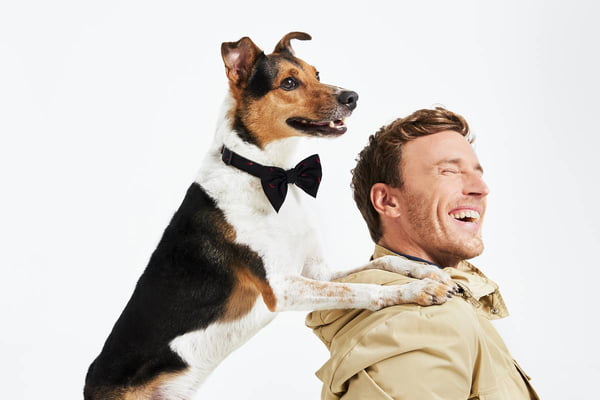 Modelo branco sorri ao lado de cachorro de médio porte com gravata borboleta - Metrópoles