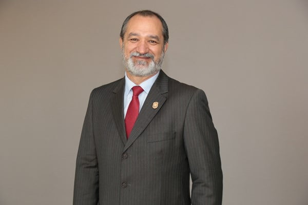 fotografia colorida mostra homem de terno escuro, gravata vermelha. Ele está sorrindo
