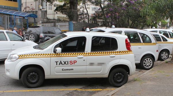 Imagem colorida com táxi da cidade de SP, um carro branco com detalhes em amarelo