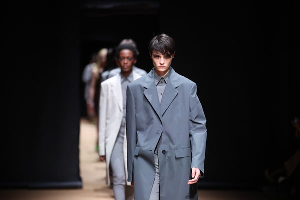 Na passarela da Prada, em fila de modelos, look com sobretudo cinza e camisa social - Metrópoles