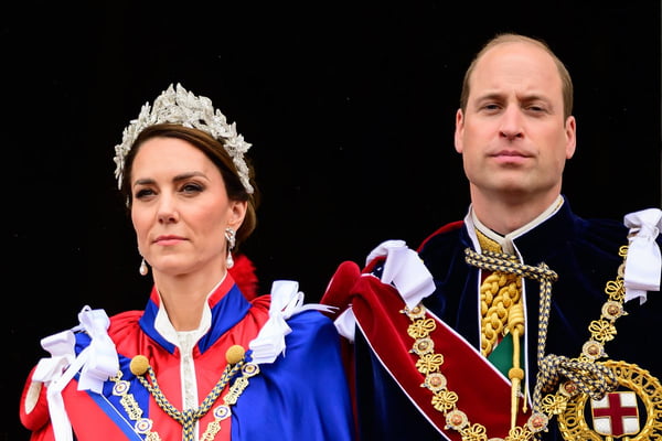 Foto colorida de mulher branca, com tiara na cabeça, capa azul e vermelha. Ela está ao lado de homem, branco e calvo, com capa azul com símbolos militares - Metrópoles