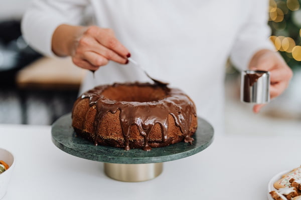 Na foto, uma pessoa colocando uma calda de chocolate em cima de um bolo - Metrópoles