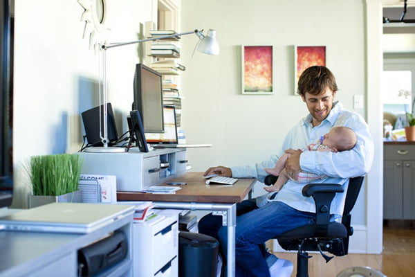 Imagem colorida de homem no home office, segurando o filho pequeno