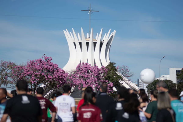 Fieis aglomerados. Catedral de Brasília e ipês rosas ao fundo