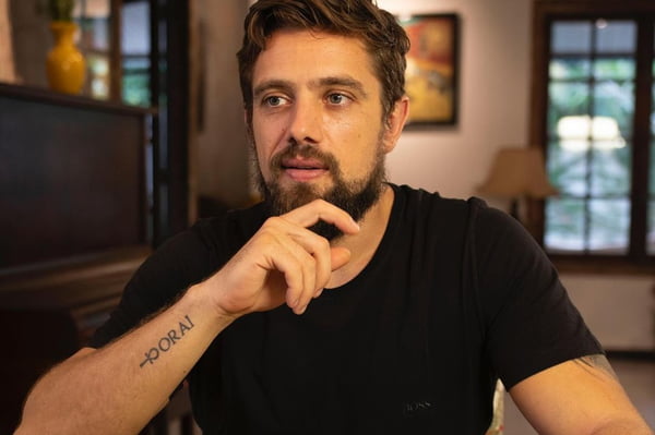 Foto colorida do ator Rafael Cardoso olhando para o nada com a mão no queixo e camiseta preta - Metrópoles