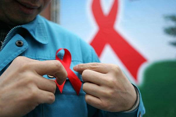 Foto mostra homem colocando um botom com o símbolo do combate À aids e ao HIV