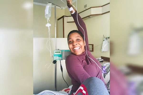 Foto mostra mulher negra sorrindo para a câmera em ambiente hospitalar. Ela tem um acesso conectado a seu braço - Metrópoles