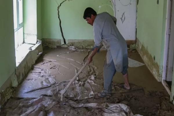 Imagem colorida de homem tentando limpar o chão após as enchentes no Afeganistão - Metrópoles