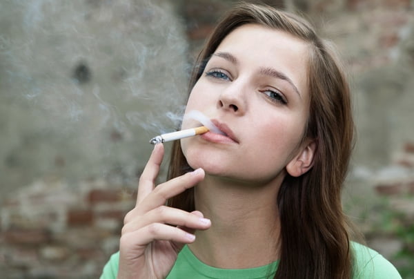 Foto mostra jovem branca com um cigarro na boca a fumar olhando para a câmera -- Metrópoles