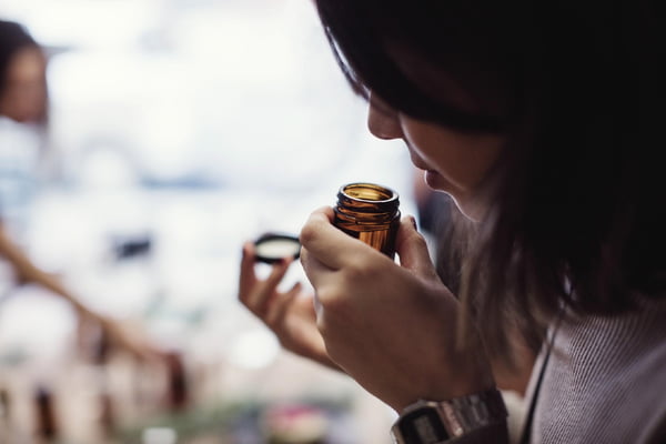 Foto mostra mulher abrindo pote de vidro de pequeno tamanho e aproximando-o de seu nariz - Metrópoles - cheiro