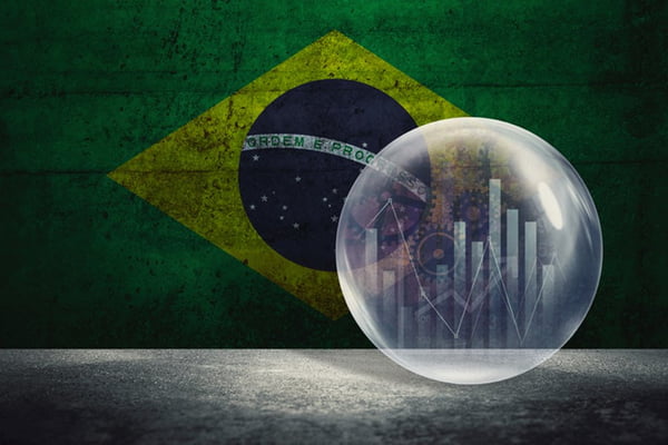 Imagem colorida da bandeira do Brasil, ao fundo. À frente dela, uma redoma branca com gráficos de indicadores econômicos dentro de um círculo - Metrópoles