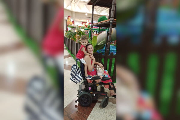Imagem colorida de mulher em cadeira de rodas com crianças abraçando por trás - Metrópoles