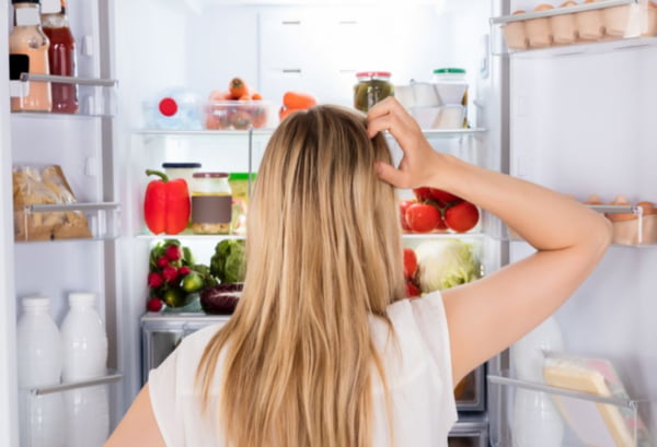 Mulher loira de blusa branca em frente a geladeira olhando o que tem dentro - Metrópoles
