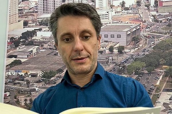 Homem branco com cabelo grisalho e camisa azul olha para baixo, lendo um livro - Metrópoles