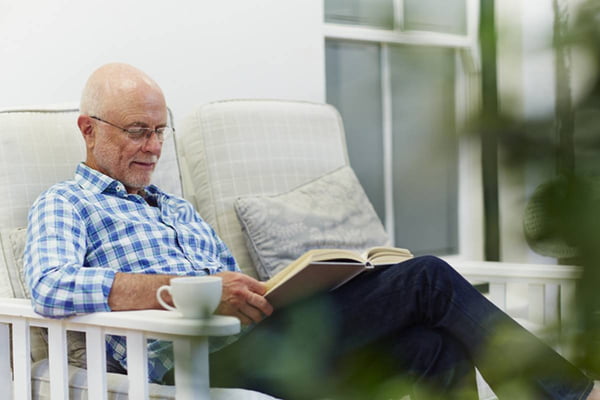 Imagem coloridade de idoso sentado em sofa enquanto lê - Metrópoles
