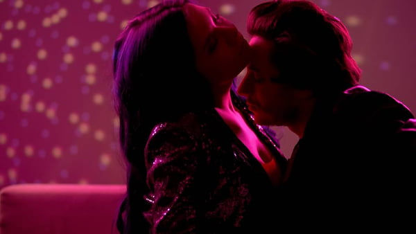 Foto colorida com efeito de luz cor de rosa de um casal se beijdando em uma festa - Metrópoles