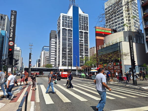 Imagem mostra pessoas cruzando avenida em faixa de pedestre - Metrópoles
