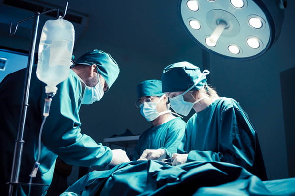 Imagem colorida de cirurgiões reundidos envolta de mesa de operação - Metrópoles