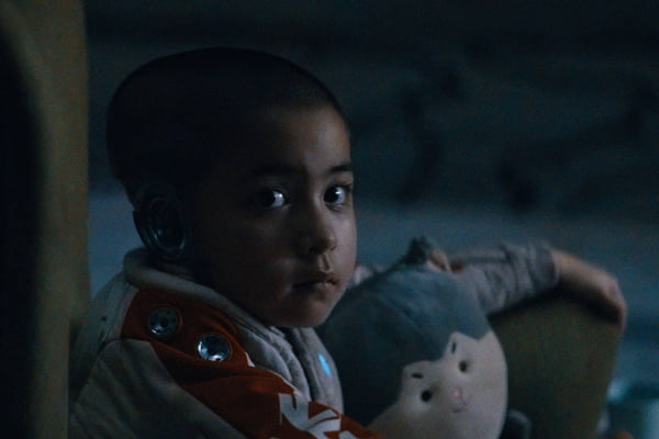 cena colorida de filme com robô criança olhando para a camera com boneca no colo - metrópoles
