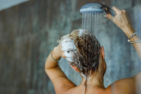 Mulher de costas lavando o cabelo em chuveiro - Metrópoles