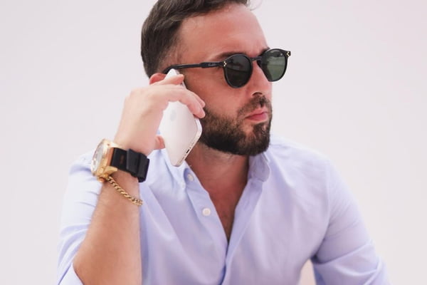 Irmão de Virginia Fonseca, William Gusmão posa de camisa social branca, óculos escuros e segurando um telefone celular - Metrópoles