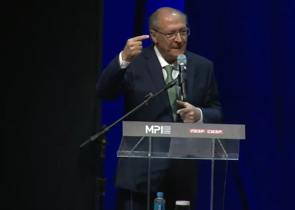 Imagem de Geraldo Alckmin, vice-presidente da República, falando ao microfone em um púlpito. Ele veste terno escuro, camisa clara e usa gravata verde e óculos - Metrópoles