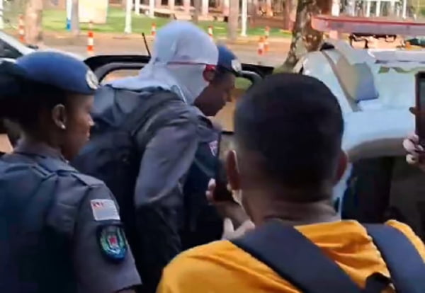 Imagem colorida mostra homem encapuzado sendo colocado em viatura da polícia. Ele é um professor da Unicamp, que ameaçou um aluno com uma faca dentro do campus da instituição - Metrópoles