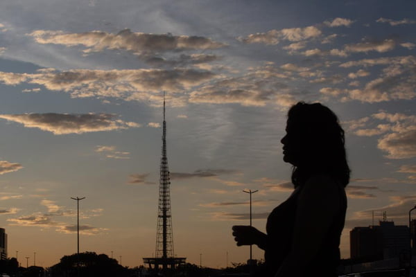 Mulher caminha no por sol do sol com a Torre de Tv ao fundo - Metrópoles