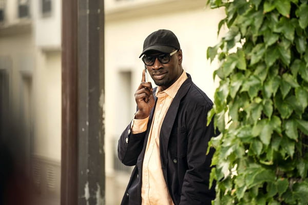 Foto colorida de Omar Sy, homem negro usando bone e jaqueta pretos - Metrópoles