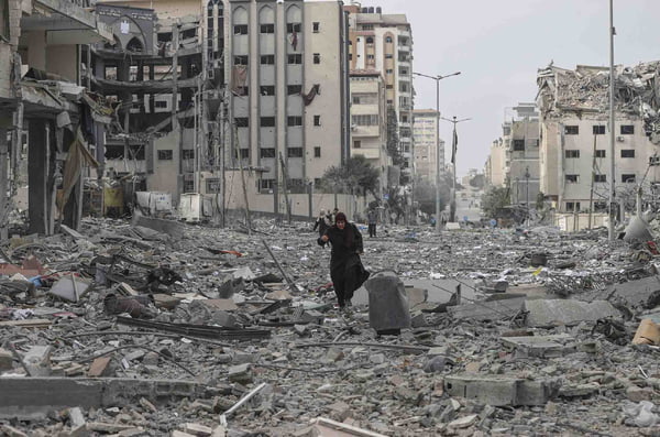 Mulher caminha entre edifícios destruídos e destroços no bairro de al-Rimal após ataques aéreos israelenses na Faixa de Gaza - Metrópoles