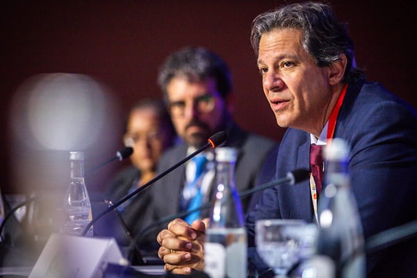 Fernando Haddad, ministro da Fazenda, participando de conferência do FMI. Ele está sentado e falando ao microfone - Metrópoles