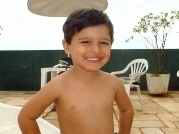 Foto colorida mostra Joaquim Ponte, menino branco, pequeno sorrindo com as mãos na cintura e cabelo preto de franja - Metrópoles