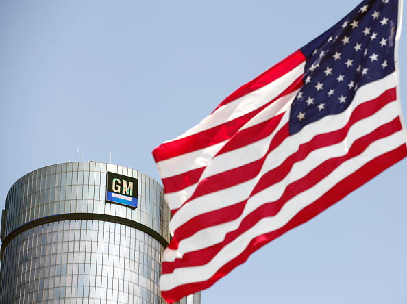 Imagem da bandeira dos Estados Unidos e, ao fundo, uma fábrica da General Motors - Metrópoles