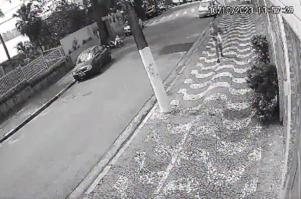 Imagem em preto e branco retirada de vídeo de câmera de segurança mostra homem abrindo sacola plástica com pedras, em calçada de São Vicente, antes de atirá-las em direção ao prédio onde Márcio França mora - Metrópoles