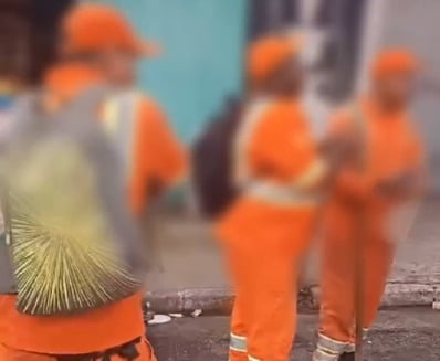 Imagem borrada de homens com uniformes laranjas de funcionários de limpeza urbana - Metrópoles
