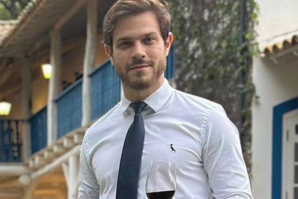 Felipe Becari posa de camisa social, gravata e uma taça de vinho na mão - Metrópoles