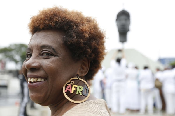 Imagem colorida de mulher negra em frente do monumento do Zumbi dos Palmares - Metrópoles