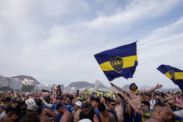 Imagem de torcedores do Boca Juniors, da Argentina, fazendo festa na praia de Copacabana, no Rio de Janeiro, com camisas do time e bandeiras com o símbolo do clube - Metrópoles