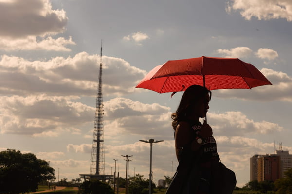 Imagem colorida de mulher se protegendo do sol com o guarda-chuva - Metrópoles