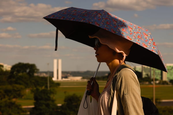 Imagem colorida de mulher se protegendo do sol com o guarda-chuva calorão - Metrópoles