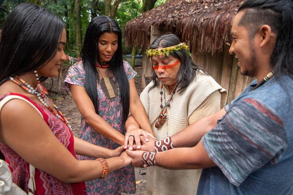 foto colorida de duas mulheres e dois homens indigenas de mãos dadas em um semi-circulo - metrópoles